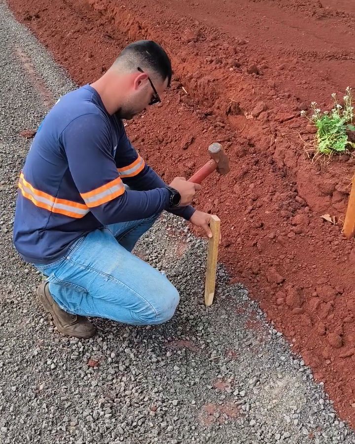 Topógrafo cravando piquete de locação ao lado da base de meio-fio em loteamento